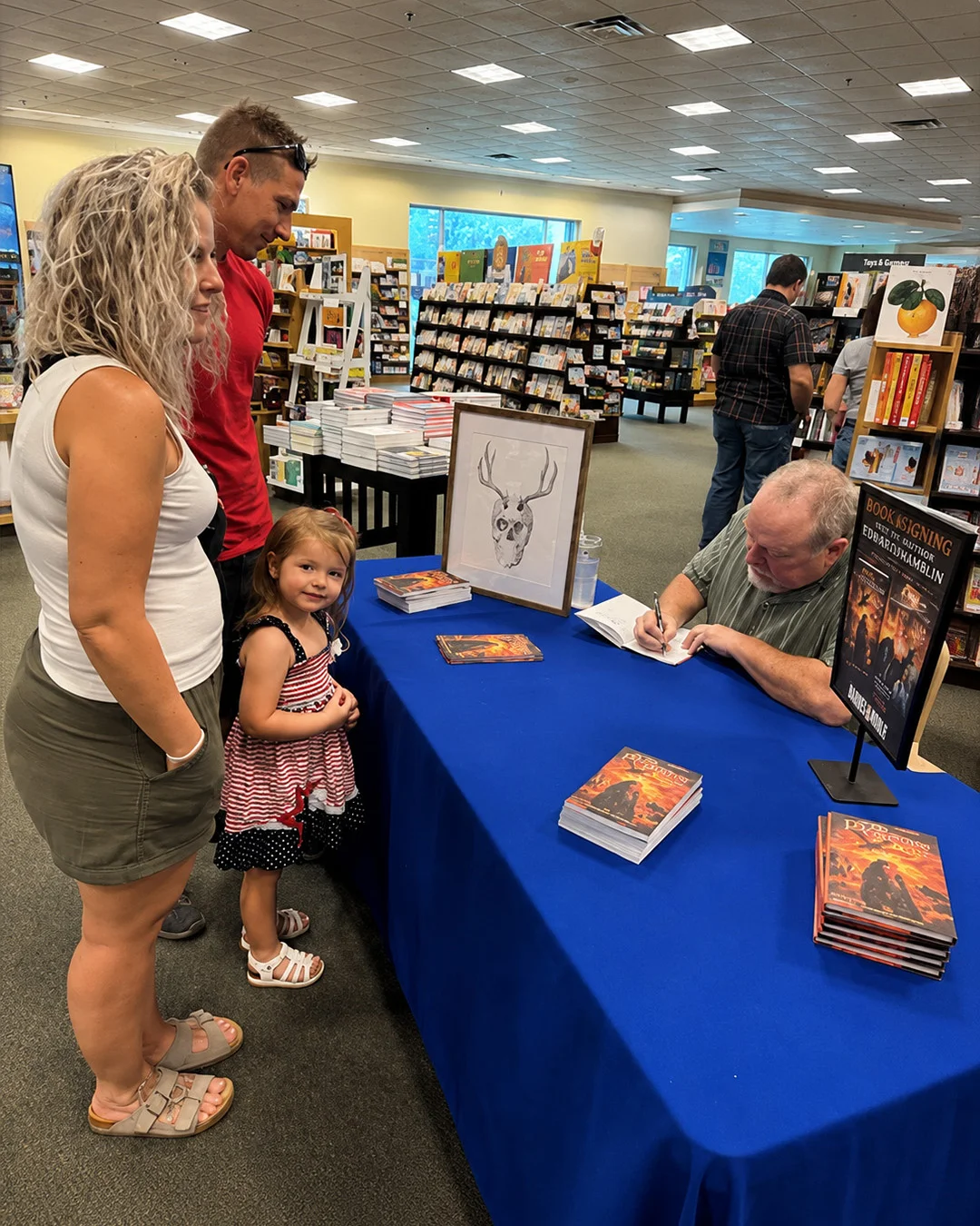 A family with a small child at the signing table, watching the author sign a copy